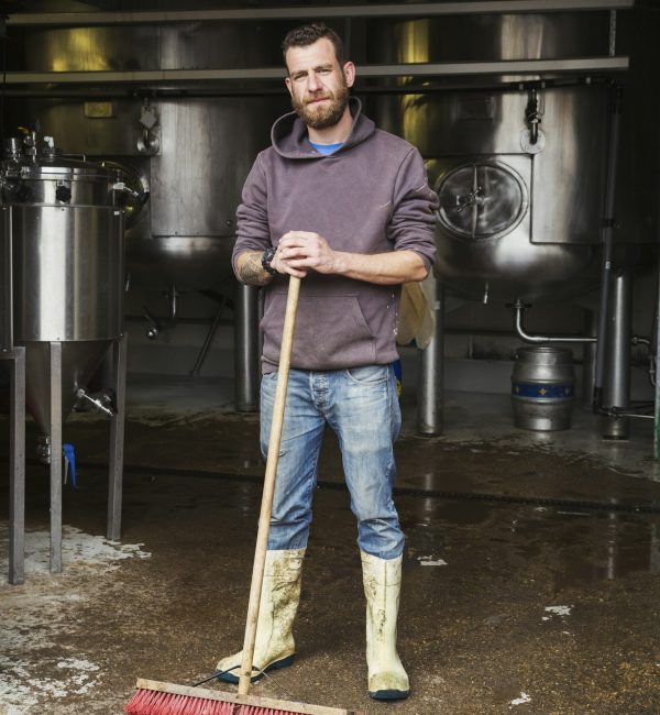 Man working in a brewery, cleaning floor with a large broom.